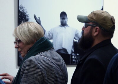 Kobieta w płaszczu i mężczyzna w czapce z daszkiem oglądają czarbo-białą fotografię z wystawy "Blisko nas".